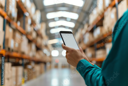 A worker in a blue smock uses a smartphone to check inventory in a warehouse.