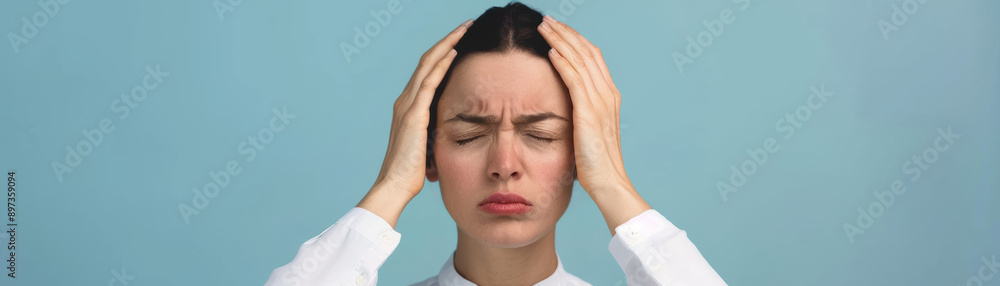 A frustrated woman in white holds her head in distress against a blue background, conveying stress and headache. A frustrated woman in white holds her head in distress against a blue background, conveying stress and headache.