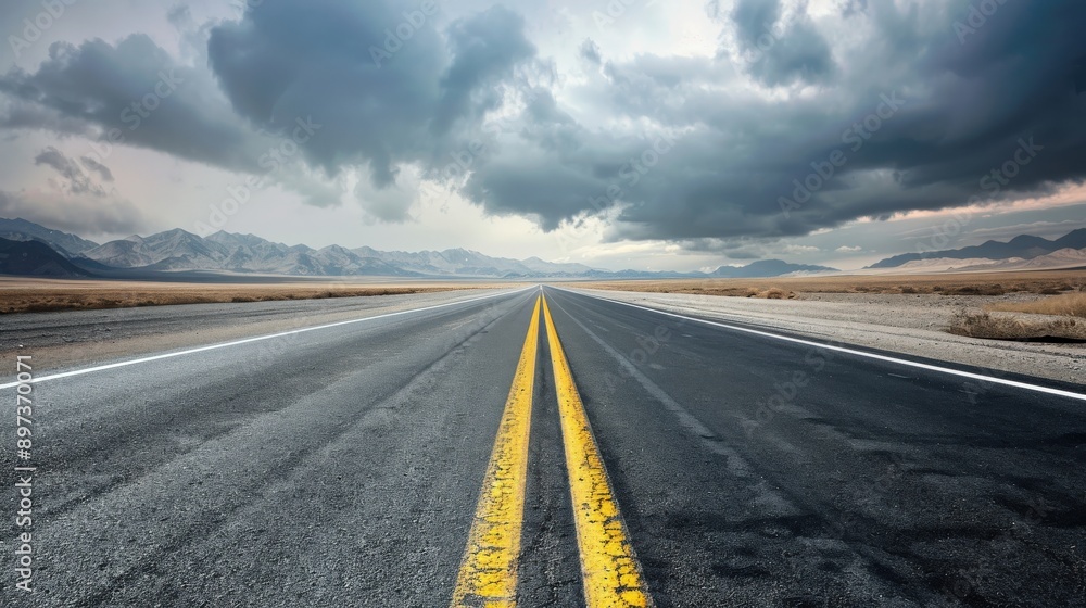 Fototapeta premium A long, empty road with a yellow line down the middle. The sky is cloudy and the road is wet