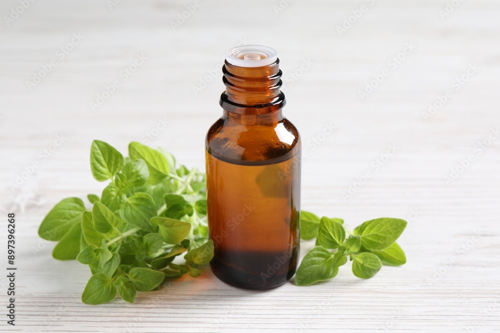 Essential oil in bottle and oregano leaves on white wooden table, closeup Essential oil in bottle and oregano leaves on white wooden table, closeup