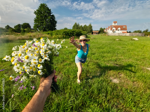 woman running across the field for a bouquet of daisies, field bouquet, happy girl, blue sky, clouds, old houses, woman in sherts, summer photo