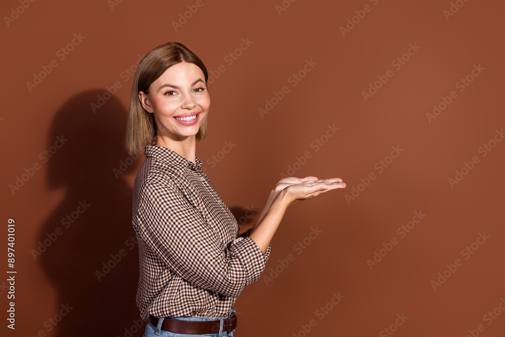 Photo of lovely adorabel positive woman wear plaid stylish clothes hold offer empty space isolated on brown color background Photo of lovely adorabel positive woman wear plaid stylish clothes hold offer empty space isolated on brown color background
