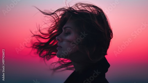 Silhouette of a person with windblown hair standing against a background with beautiful pink and purple hues of a sunset, creating a sense of serenity and freedom.