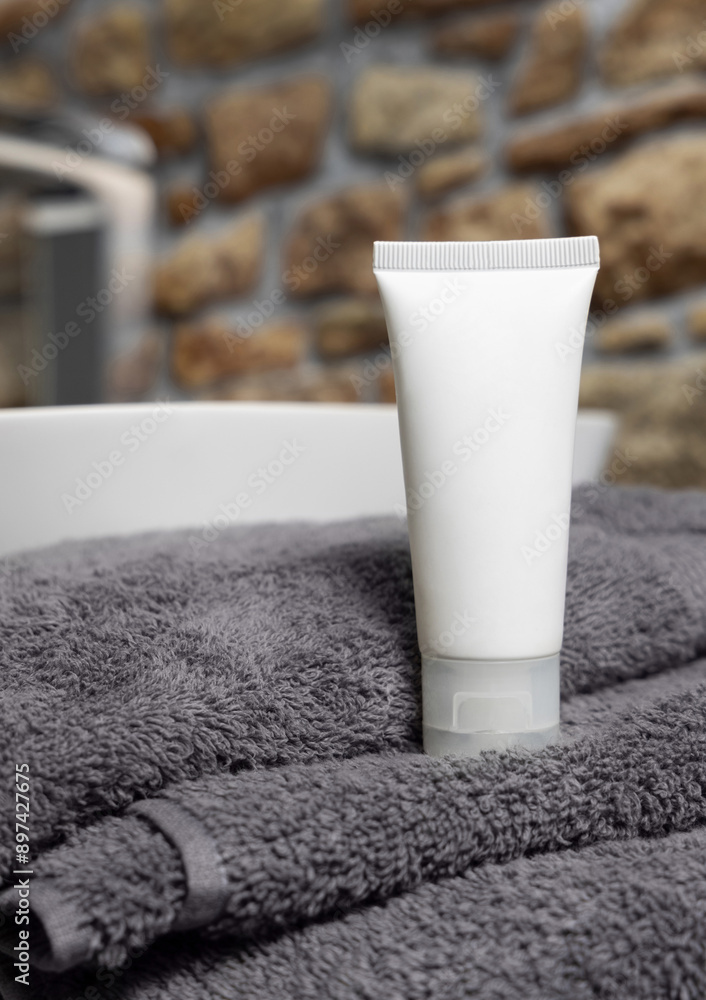 White cosmetic tube on dark grey folded towel near vessel basin against stone wall, mockup White cosmetic tube on dark grey folded towel near vessel basin against stone wall, mockup