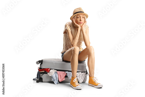 Pensive female tourist sitting on a suitcase full of clothes photo