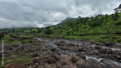 Stream flowing over small rocks with Shayadri hill in background, lush greenery during monsoon. photo