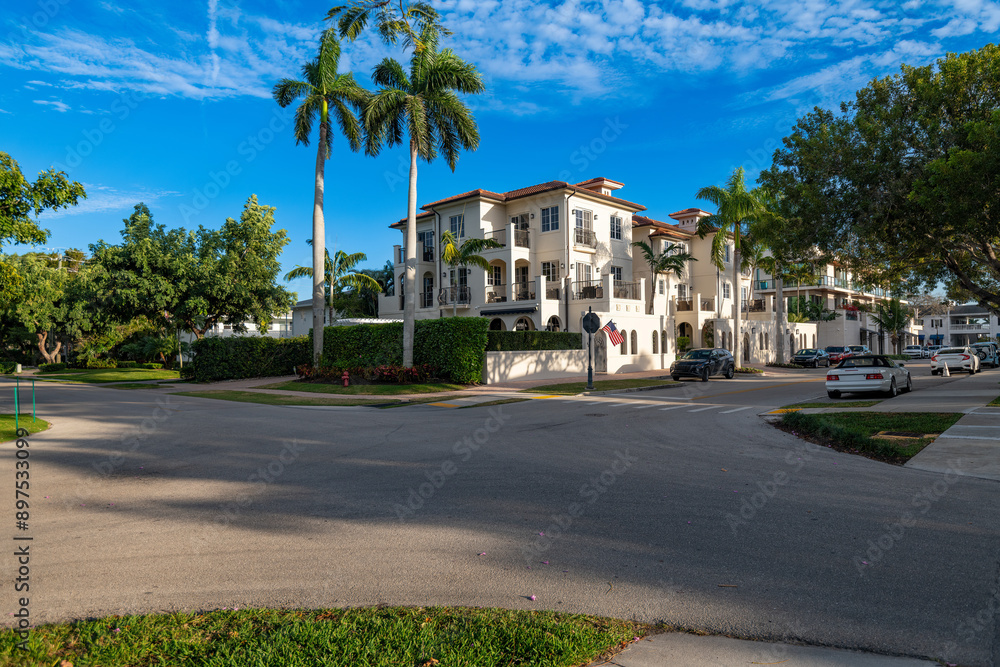 A street corner in a wealthy neighborhood in downtown Naples, with a large white building, palm trees, and a few cars on a sunny day. A street corner in a wealthy neighborhood in downtown Naples, with a large white building, palm trees, and a few cars on a sunny day.