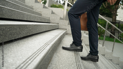 Skilled business man walking up stairs at park or city while holding bag in the hand Professional project manager going to workplace. Represent growth, getting promotion, increasing skill. Exultant.