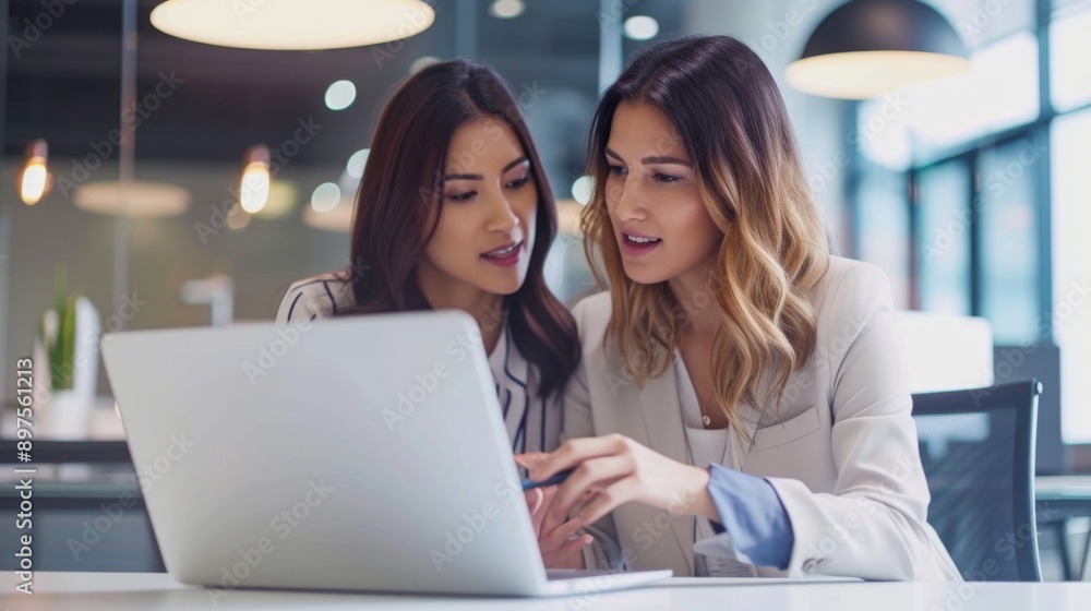 Two professional women working together on a laptop in a modern office setting Two professional women working together on a laptop in a modern office setting