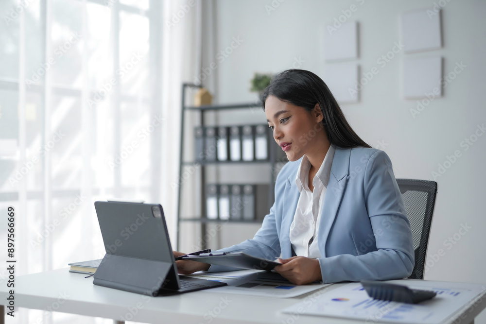 Businesswoman is reviewing documents and working with a digital tablet at her desk in the office Businesswoman is reviewing documents and working with a digital tablet at her desk in the office