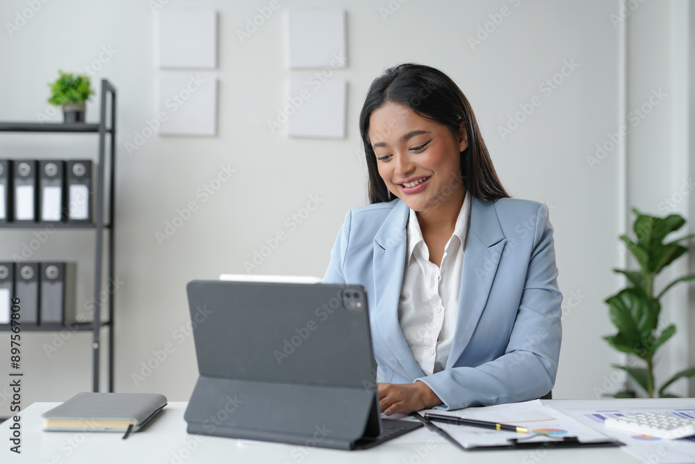 Asian businesswoman is smiling while working on a tablet computer at her desk in a modern office Asian businesswoman is smiling while working on a tablet computer at her desk in a modern office