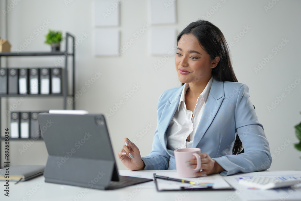 Smiling businesswoman working remotely and drinking coffee, analyzing financial charts and reports on a digital tablet Smiling businesswoman working remotely and drinking coffee, analyzing financial charts and reports on a digital tablet