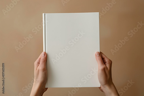 A person holding up an empty white book with a plain cover, showing the blank page for writing space and text on a beige background photo