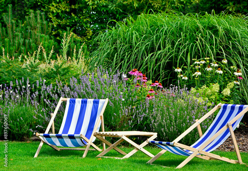Obraz na płótnie leżaki w biało-niebieskie pasy w ogrodzie, leżaki w ogrodzie, kącik wypoczynkowy z leżakiami, blue and white striped deckchairs in the garden, deckchairs in the garden, empty deck chairs, seating area w salonie