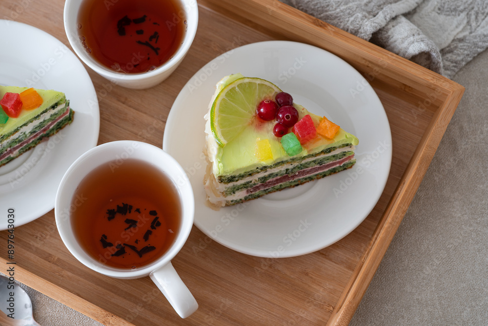 Two slices of fruit cake with citrus and berry toppings, placed beside cups of tea on a wooden tray, creating a cozy and inviting setting Two slices of fruit cake with citrus and berry toppings, placed beside cups of tea on a wooden tray, creating a cozy and inviting setting