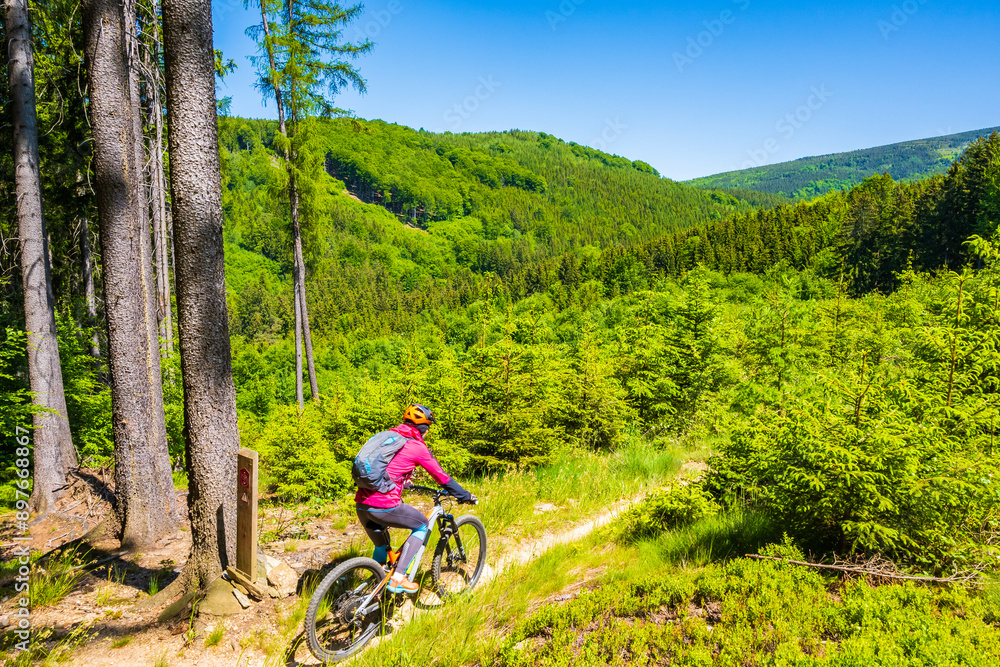 Woman with backpack riding mountain bike on single track trail among green hills in Jizera Mountains, Singletrk pod Smrkem Czech Republic