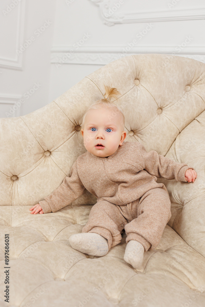 Fototapeta premium A child in beige overalls is sitting on a sofa. Warm clothes for babies