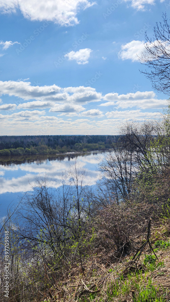Panoramic view of river bend, forest and blue sky. Beautiful reflection of white clouds in water at sunny day. Aerial view of picturesque background
