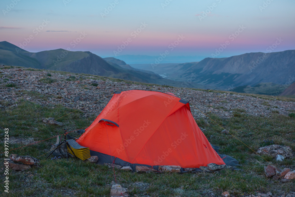 Orange tent on grassy stony pass with view to valley and mountain range ...