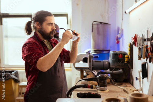 Carpenter in woodworking shop checking for scratches on protection glasses before assembling furniture. Cabinetmaker ensuring safety equipment is not damaged before starting work