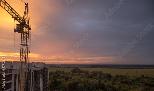 A construction crane against a golden sunset, there are trees and a field