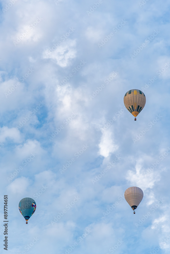 Fototapeta premium group of 3 coloured hot air balloons flying through the cloudy skies in a competition