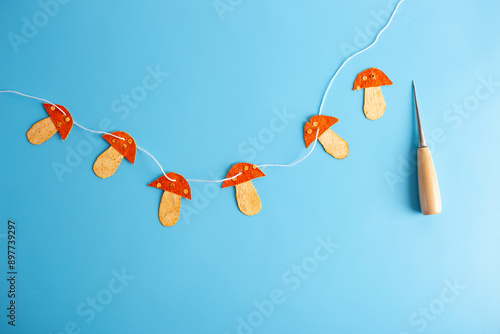 a string of orange mushrooms made of dried tangerine peel sitting on top of a blue surface, folk art, awl photo