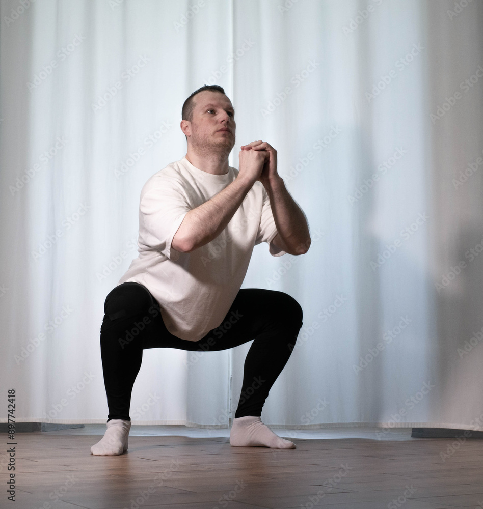 Obraz premium Home workouts in yoga poses. A man performs sports exercises, warming up the body of his arms and legs, A male athlete stretches.