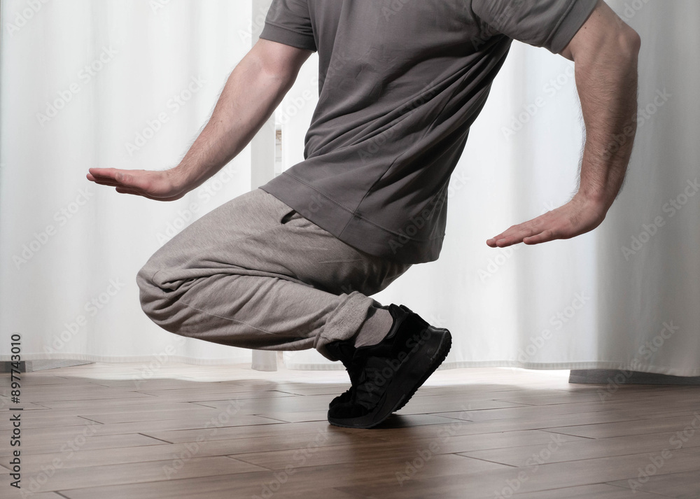 Naklejka premium Dance in motion, pose of a man in hip-hop style clothes. Sports dancing guy in training poses. Dance training at home.