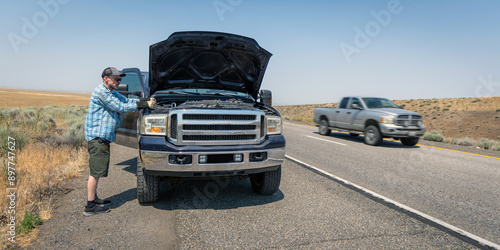 Blue pickup truck breaks down on the shoulder of a freeway while owner tries to assess the problem.