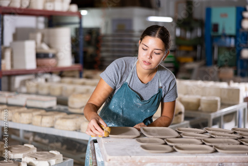 Young woman ceramist polishing new clay plates with sponge in workshop. photo