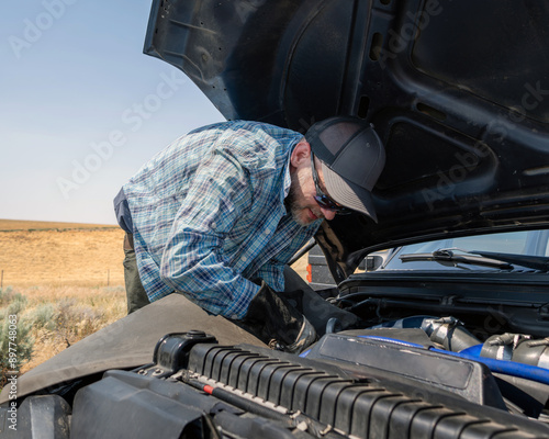 Blue pickup truck breaks down on the shoulder of a freeway while owner tries to assess the problem.