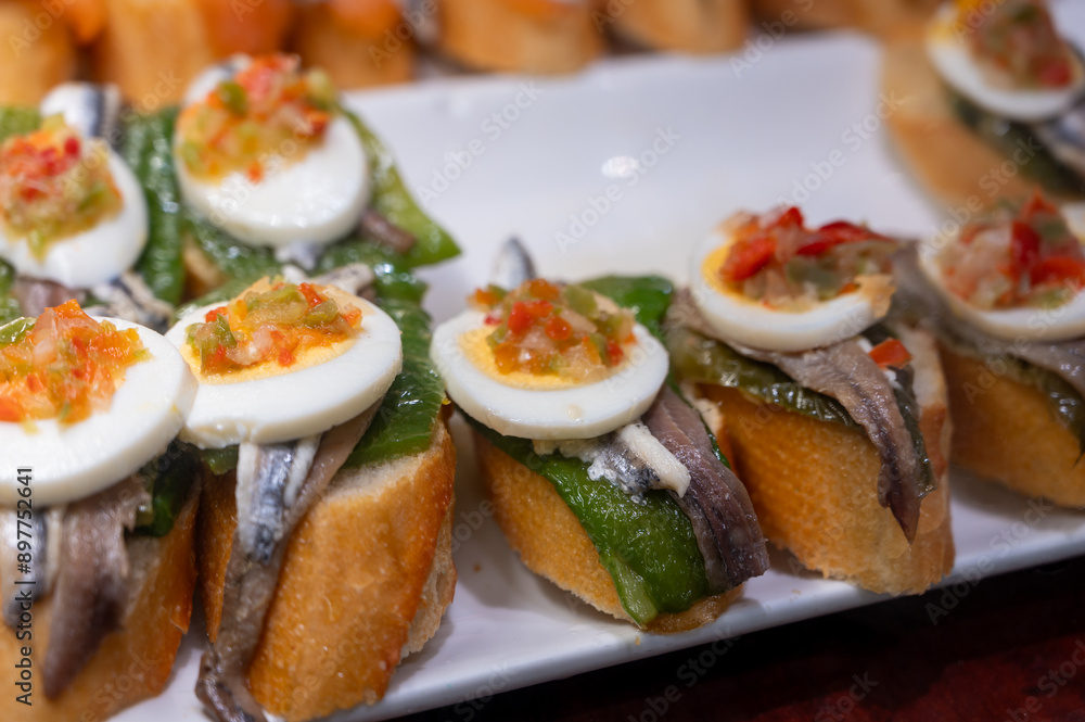 Typical snack of Basque Country, pinchos or pinxtos skewers with small pieces of bread, sea food, eggs, cheese, jamon served in bar in San-Sebastian or Bilbao, Spain, close up Typical snack of Basque Country, pinchos or pinxtos skewers with small pieces of bread, sea food, eggs, cheese, jamon served in bar in San-Sebastian or Bilbao, Spain, close up