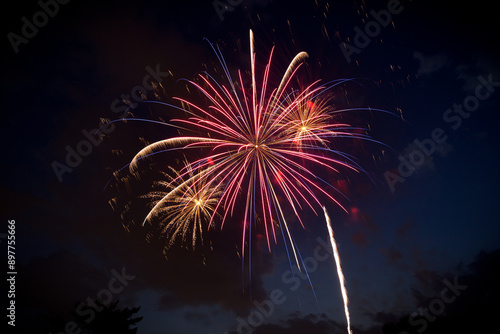 A large red and blue firework and two smaller yellow gold fireworks at dusk against a partially cloudy night sky. Copy space.