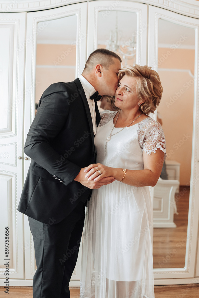 A man kisses a woman's cheek. The woman is wearing a white dress A man kisses a woman's cheek. The woman is wearing a white dress