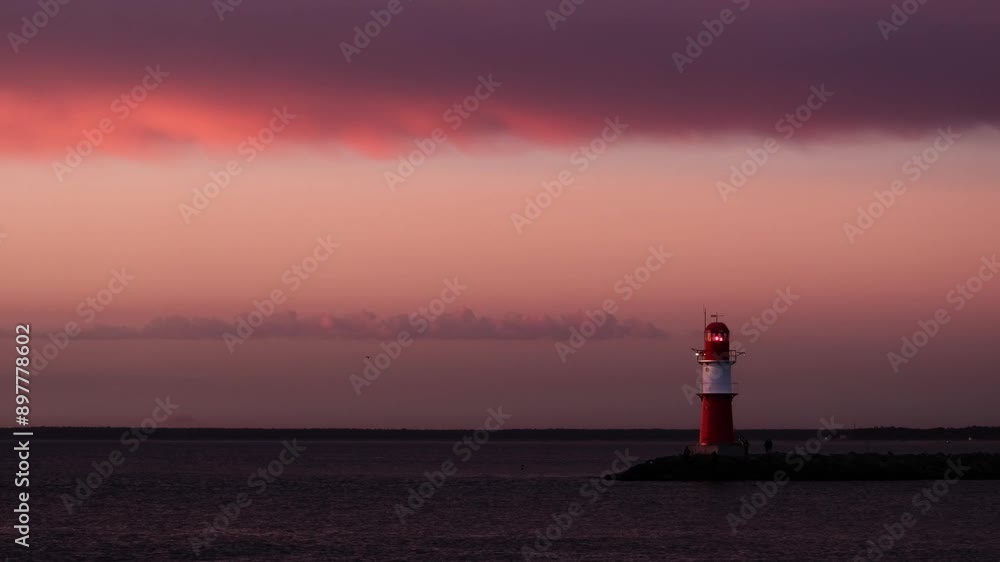 Red light beams of the lighthouse in Warnemünde, Germany. Objects of water transportation, navigation on the Baltic Sea at night concept. Minimalistic and colourful sunset footage with copy space. Red light beams of the lighthouse in Warnemünde, Germany. Objects of water transportation, navigation on the Baltic Sea at night concept. Minimalistic and colourful sunset footage with copy space.