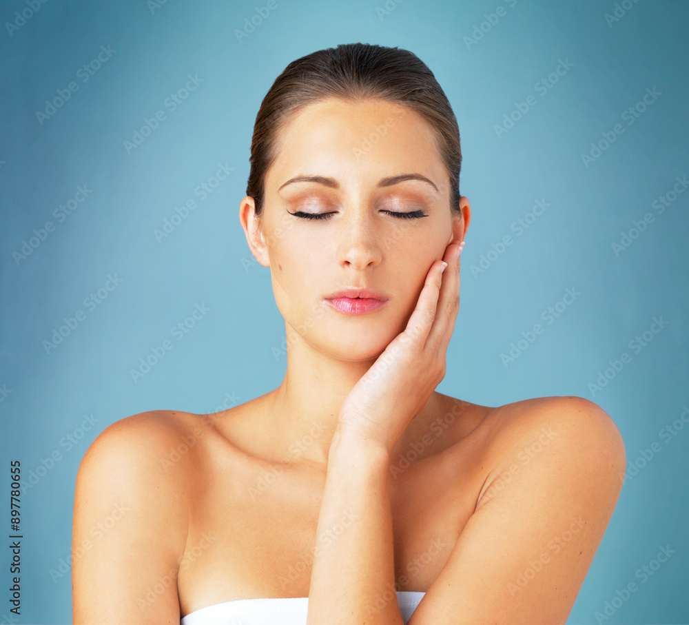 Woman, beauty and touching face for skincare with natural makeup, wellness and glow in studio. Female person, dermatology and soft skin for collagen cosmetics, shine and health by blue background Woman, beauty and touching face for skincare with natural makeup, wellness and glow in studio. Female person, dermatology and soft skin for collagen cosmetics, shine and health by blue background