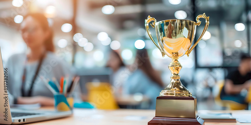 A gold trophy sits on a table in front of a woman. The trophy is the symbol of achievement and success. The woman is likely the recipient of the trophy