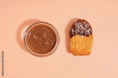 Tasty madeleine and bowl with chocolate paste on orange background photo