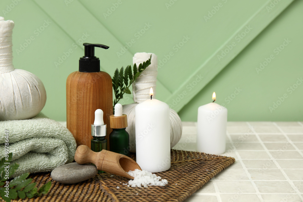 Set of spa supplies with different cosmetic products, herbal bags, fern branches and burning candles on beige tile table Set of spa supplies with different cosmetic products, herbal bags, fern branches and burning candles on beige tile table
