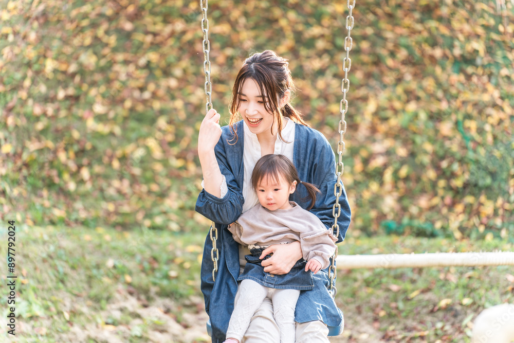 Fototapeta premium 秋の公園でブランコに乗って遊ぶ親子・ママ友・子供(幼児・ピクニック・育児・子育て)