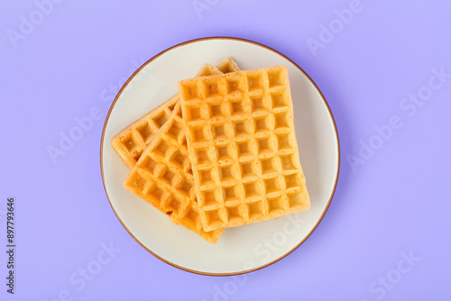 Tasty Belgian waffles in plate on lilac background. Top view