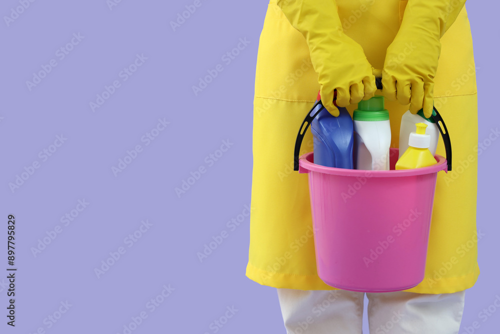Female janitor with bucket of cleaning supplies on lilac background, closeup Female janitor with bucket of cleaning supplies on lilac background, closeup