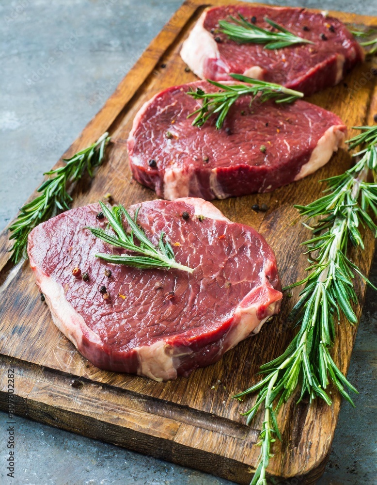 Raw beef steaks with herbs and spices ready for cooking are on wooden board. Raw beef steaks with herbs and spices ready for cooking are on wooden board.