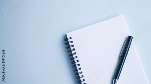 Blank notepad with a pen is laying on a blue background, providing a clean and minimalist backdrop for taking notes or brainstorming ideas