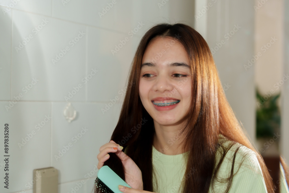 Young Asian girl brushing long straight brown hair in bathroom. Wearing light green ribbed top. Indoor setting with tiled walls. Expressing joy and self-care in morning routine. Young Asian girl brushing long straight brown hair in bathroom. Wearing light green ribbed top. Indoor setting with tiled walls. Expressing joy and self-care in morning routine.