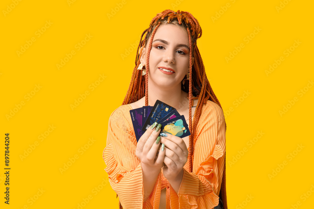 Obraz premium Portrait of pretty young woman with dreadlocks and credit cards on yellow background