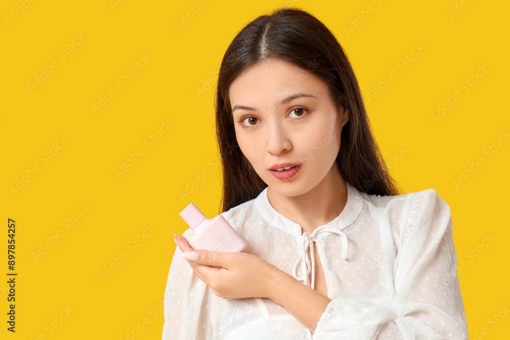 Beautiful young Asian woman with pink bottle of perfume on yellow background Beautiful young Asian woman with pink bottle of perfume on yellow background