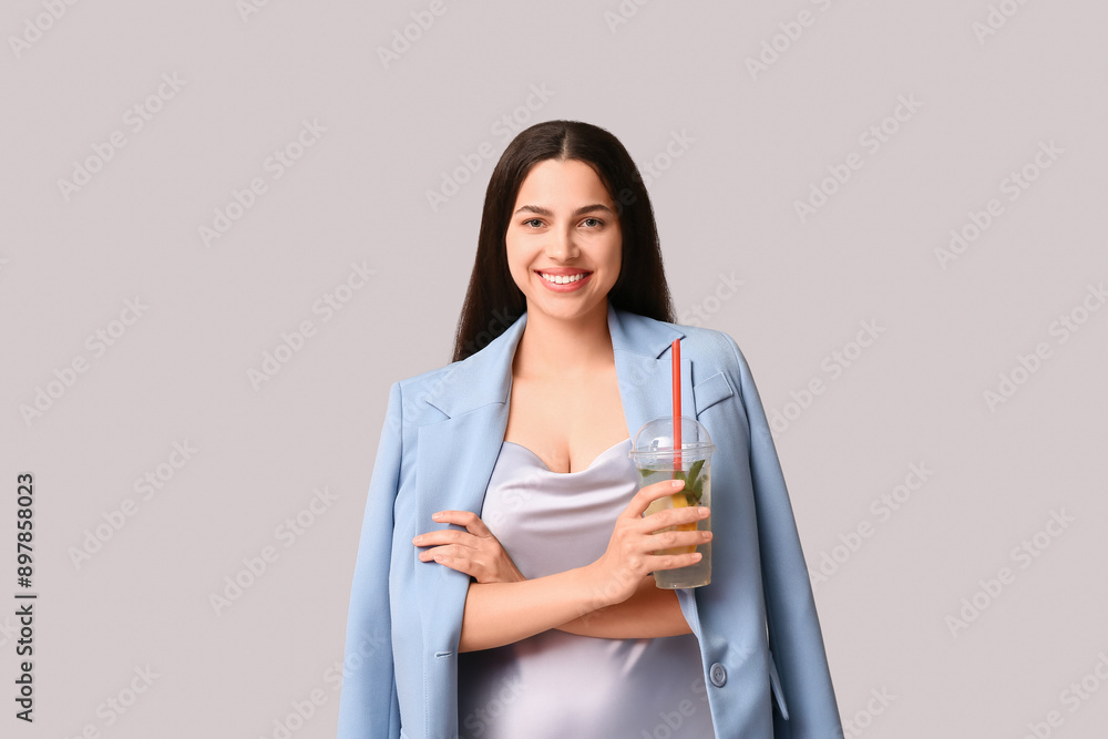 Beautiful young happy woman with cup of fresh lemonade on grey background Beautiful young happy woman with cup of fresh lemonade on grey background