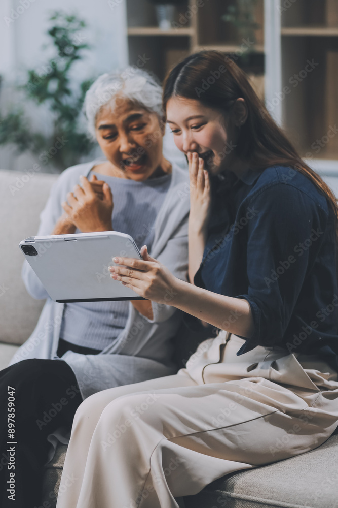 Happy grownup daughter showing content on tablet to mature mother. Two family generations women with digital computer gadget resting on couch together, watching videos, making video call